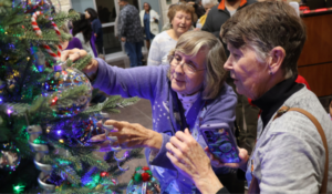 Mary Kay Thomas (r) places an ornament honoring her daughter Melissa on the Giving Tree