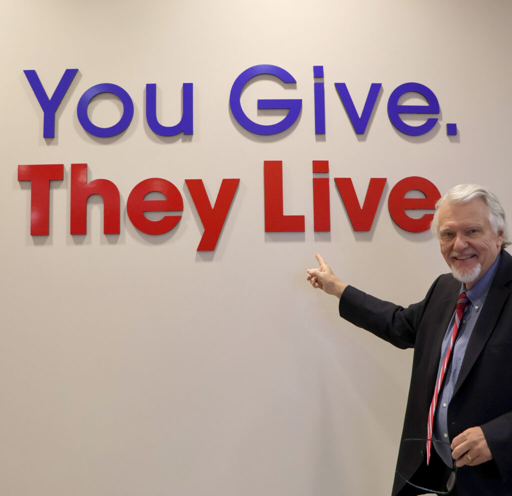 George Muller points to the You Give, They Live sign in the Donor Pavilion.