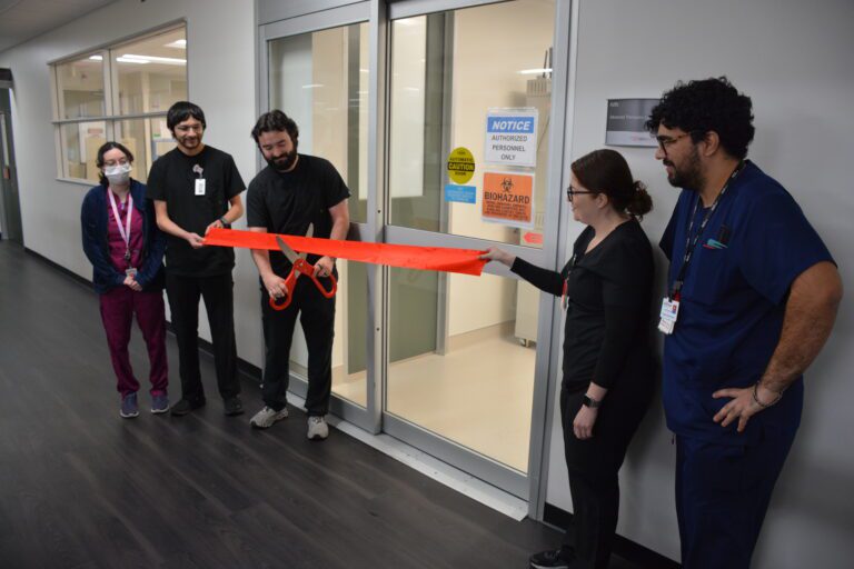 Medical staff cutting ribbon outside laboratory door