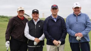 Four men posing with golf clubs on course