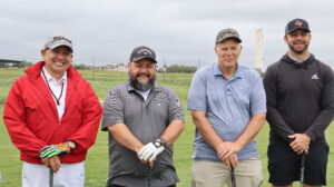 Four men posing with golf clubs on course