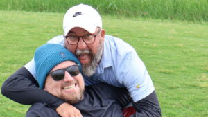 Two men playfully hugging on grassy field