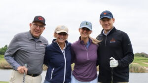 Four golfers smiling on a scenic golf course.