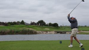 Golfer swinging club near water hazard