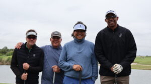 Four men posing with golf clubs on course