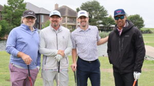Four men posing with golf clubs outdoors