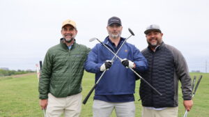 Three men posing with golf clubs outdoors